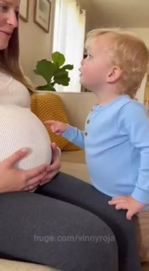 Pregnant woman smiling as a toddler points to her belly and asks if she ate the baby.
