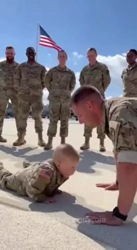 Child in military uniform leading an adult in push-ups on an airfield with an American flag.