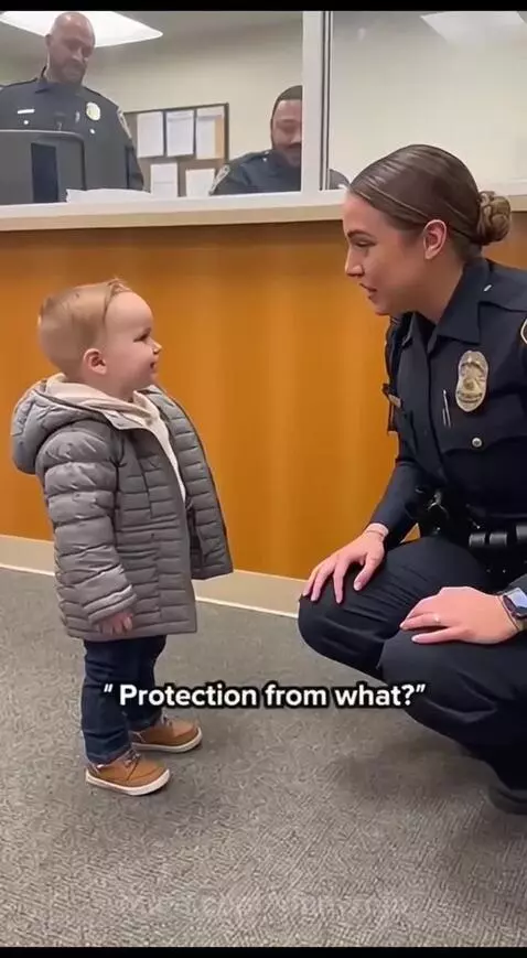 Police officer smiling while kneeling and talking to a young boy at a police station.
