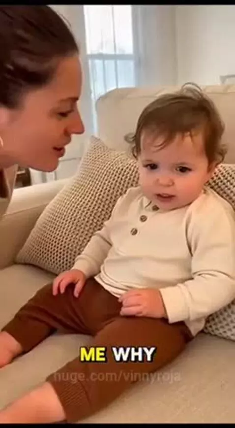 A baby sitting on a couch, playfully pushing away a woman's face and laughing.