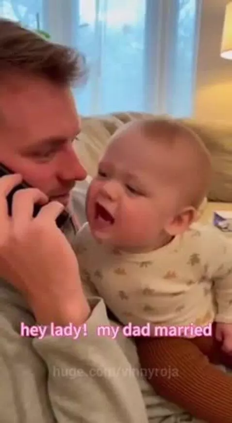 Baby sitting on dad's lap, looking intently at a phone with a funny expression.