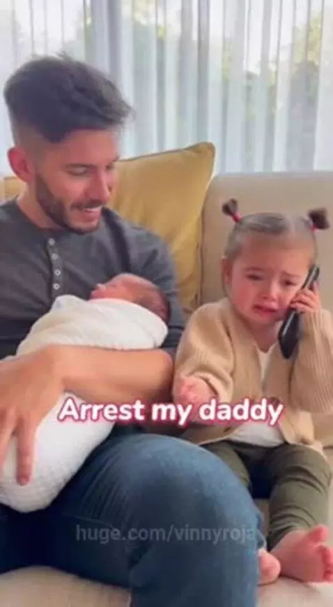 A young girl crying and holding a phone, upset that her dad is paying attention to her new baby sibling.
