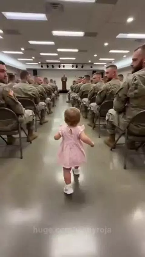 Baby girl in pink dress running to hug emotional soldier father in uniform.