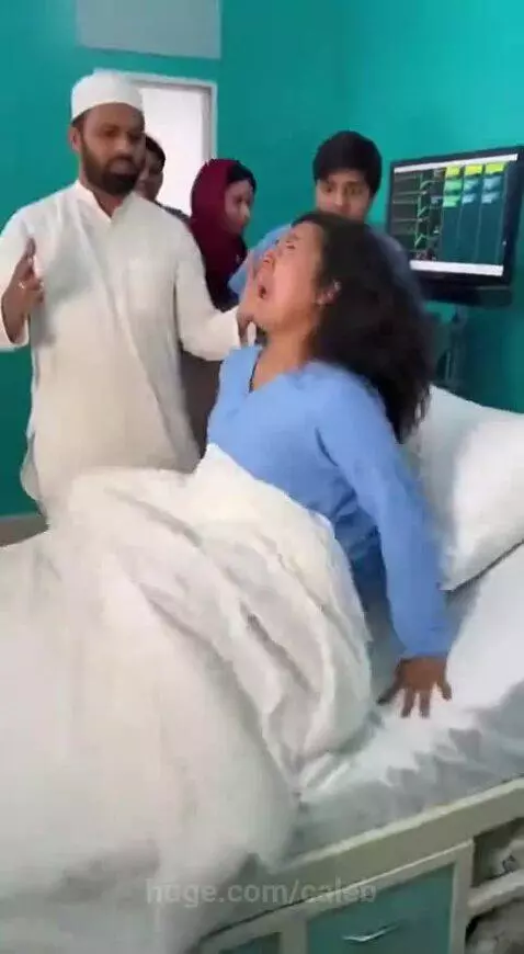 Woman in hospital gown clinging to a wall while people in traditional attire and medical scrubs look on in shock.