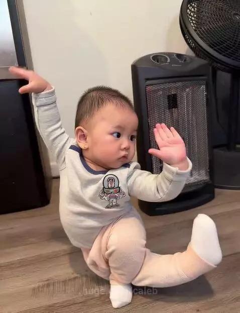 Baby in Buzz Lightyear shirt performing martial arts poses and kicks on a wooden floor.