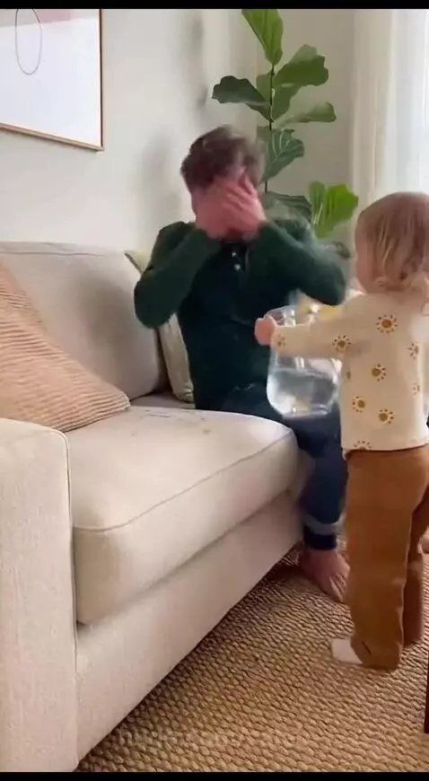 Child pouring water on a man's head, who looks surprised.