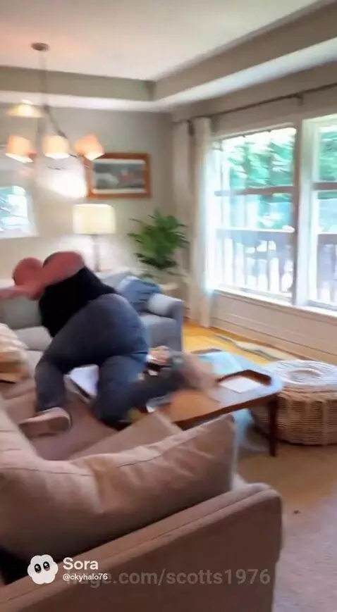 Bald man in black t-shirt playfully running with orange-handled scissors, jumping over a couch.