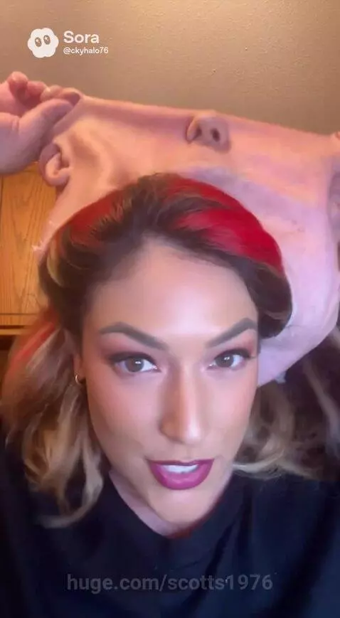 Woman with long wavy blonde and red hair smiling after removing a bald, featureless mask.