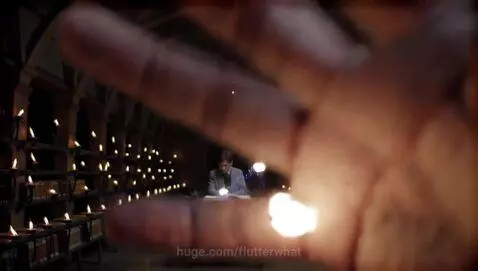 Man in a suit in a dimly lit library, surrounded by flames and swirling blue particles, manipulating light.