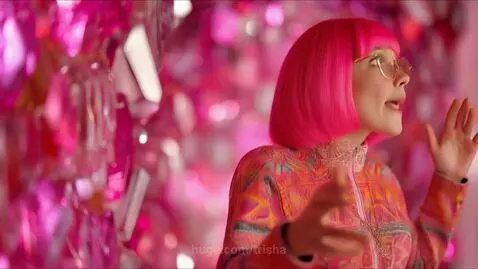 Woman with pink hair singing in a surreal mine with glowing pink crystals and a drummer in a glowing suit.