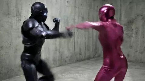 A metallic pink robot fights a dark purple robot with blue glowing eyes in a concrete room, exchanging punches and energy blasts.