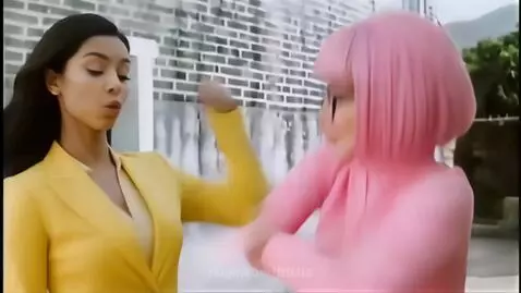Two women in yellow and pink suits sparring with martial arts moves in front of a brick wall.