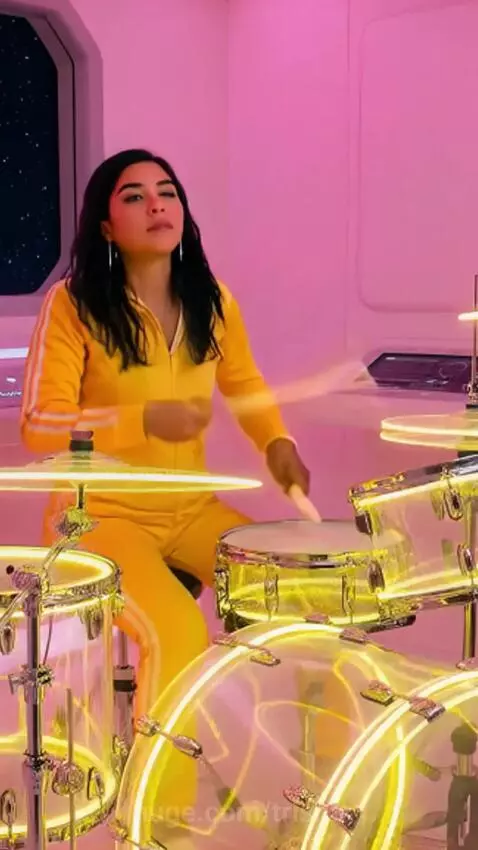 Futuristic pink UFO flying over a house, glowing control panel, and a woman playing a transparent drum set.