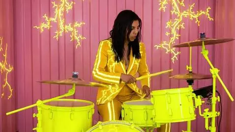 Futuristic music video scene with pink and neon yellow, featuring characters with pink hair, playing instruments, and grey aliens.
