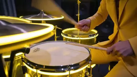 Lead singer with pink hair and suit performs with a pink guitar in a grand cathedral setting.