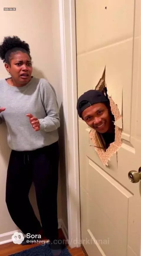 Woman with curly hair looks terrified as a man's head pops through a jagged hole in a white door.