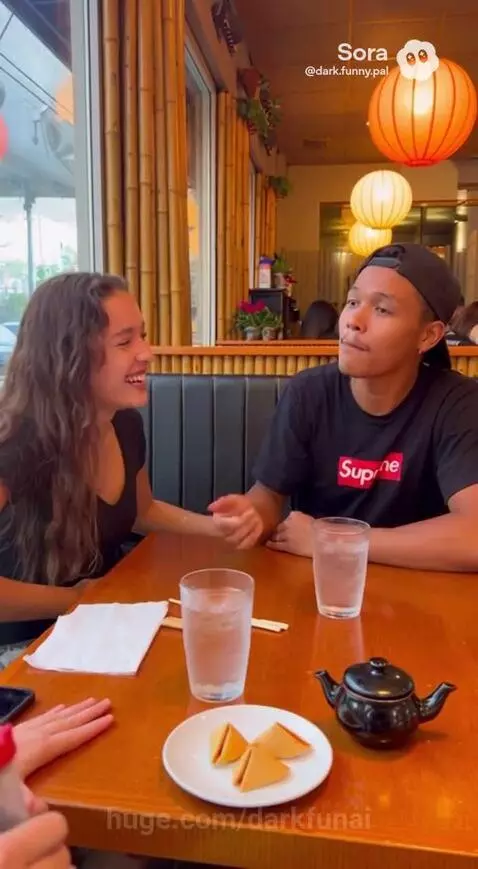 Man and woman laughing at a restaurant table with fortune cookies and drinks.