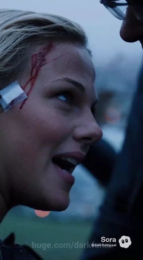 Woman with head injury being tended to by a man, with city and ocean view in the background.