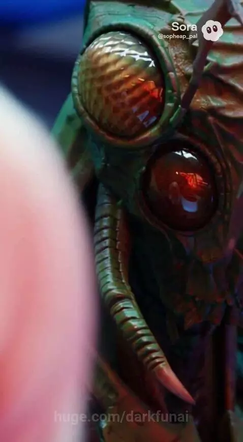 Blonde woman in grey hoodie with a large green insectoid alien in a futuristic room with blue glowing consoles.