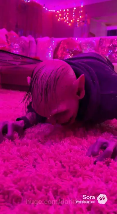 Gollum-like character crawling on a pink carpet under disco lights, wearing a detailed costume.