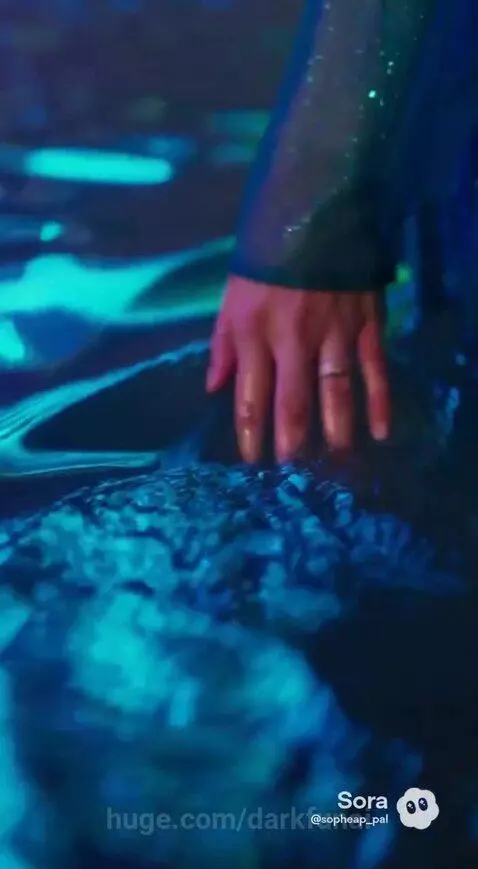 Woman in a teal dress walks towards a glowing waterfall, then performs on stage with a guitarist.