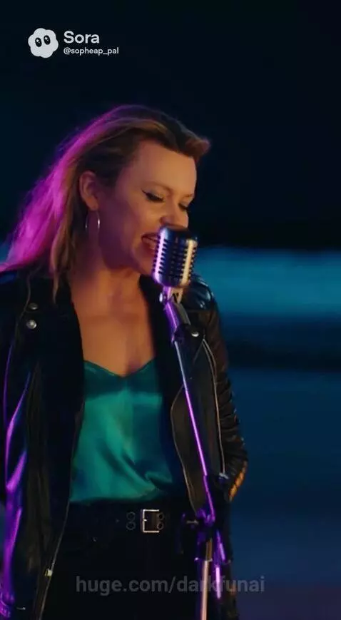 Male and female singers performing a romantic duet on a beach at night, lit by string lights and a bonfire, with the ocean and moon behind them.