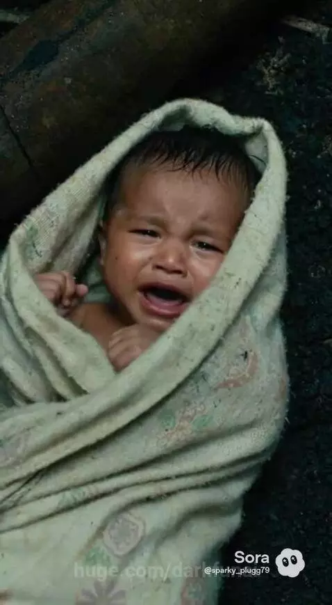 Soldier in uniform holding a baby amidst a war-torn village with burning huts.