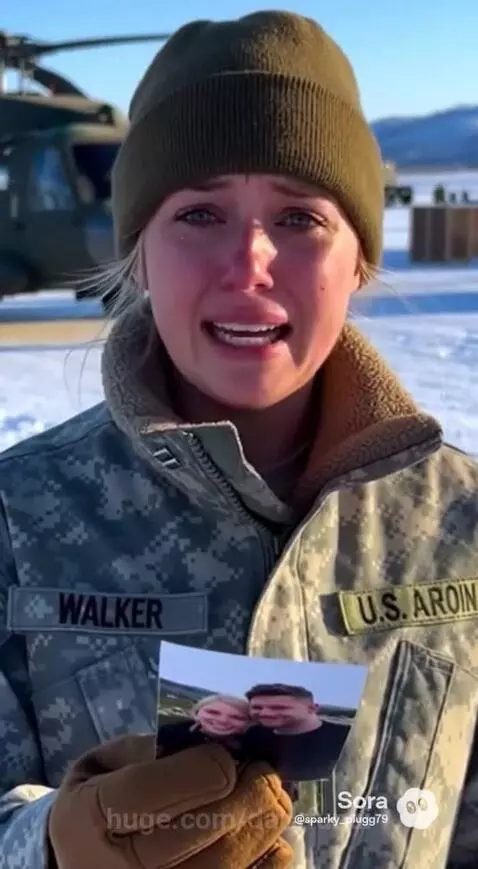 Crying woman in military uniform with beanie in snow, helicopter in background.