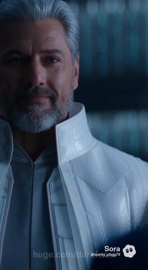 Woman with tears in her eyes in a blue dress, approached by a man in a textured coat.