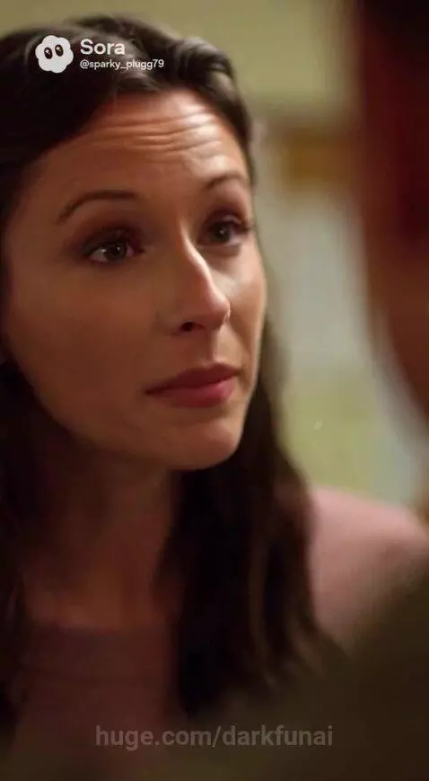 Woman in pink dress and man in military shirt discuss a secret, with a sleeping baby nearby.