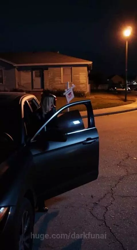 A dark cyborg with glowing eyes stands in a dimly lit room, looking at a 'For Sale' sign.