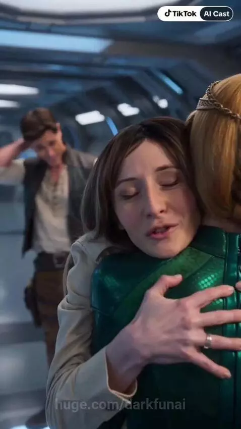 Woman in beige jacket hugs woman in futuristic green suit with golden headpiece on a spaceship.