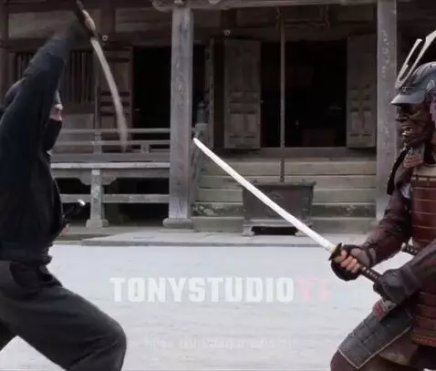 Ninja in black fighting a samurai in red and brown armor with a horned helmet on gravel.