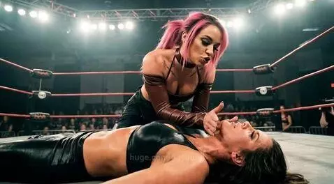 Wrestler Dakota Kai with pink hair taunting opponent Mickie James on the mat.