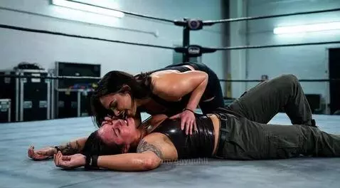 Wrestler Skye Blue leans over a defeated Kris Statlander in the ring, smiling before a kiss.