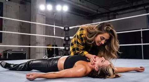 Wrestler Britt Baker kisses Jamie Hayter on the mat after a betrayal, with a smirk.
