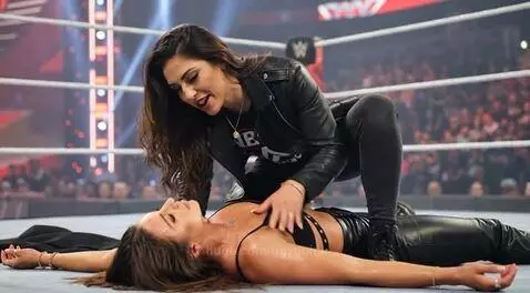 Woman in leather kneeling over another woman in a wrestling ring, about to kiss her.