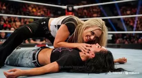 Blonde wrestler leans over and kisses a dark-haired unconscious wrestler on the mat.