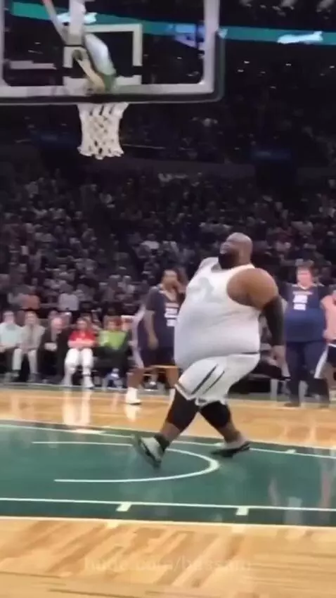 A large basketball player performing a powerful dunk with the ball.