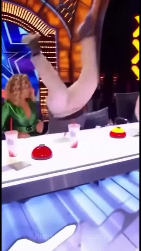 A young man on a talent show stage looking frustrated after judges buzz him, with security restraining him.