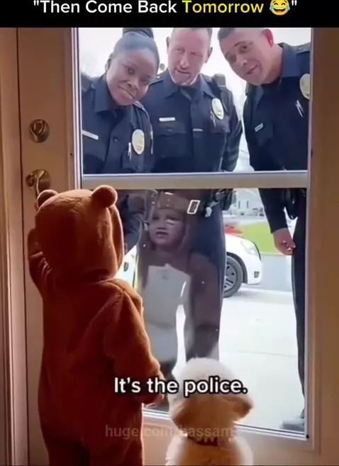 Baby in a brown bear costume looking through a glass door at smiling police officers.
