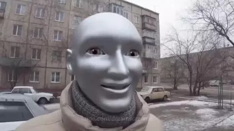 Close-up of a person wearing a bald, silver mask with wide eyes and an open mouth, speaking excitedly.