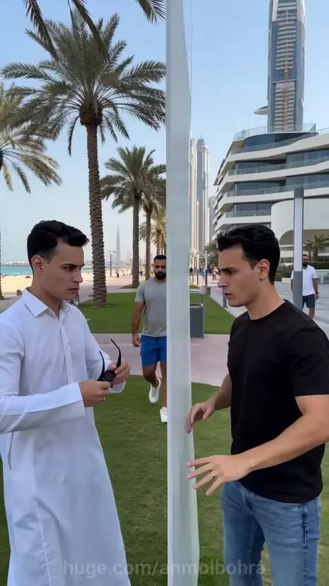 Two men in a prank, one in a white thobe, the other in a t-shirt, appearing as a mirror image with synchronized actions.