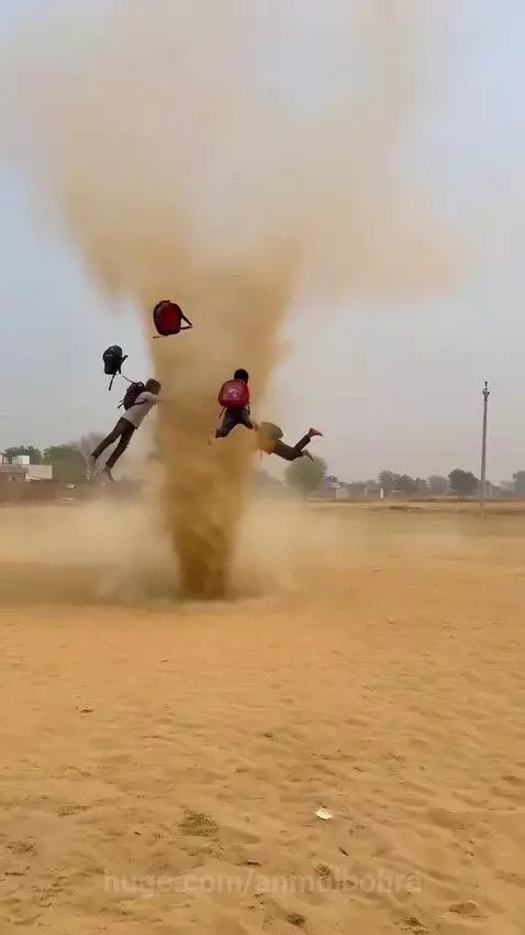 Children with backpacks running into and being lifted by a large dust devil in a sandy field.