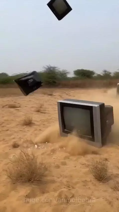 Multiple old CRT televisions falling and crashing into a dusty, barren field.
