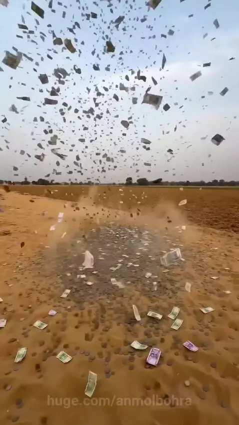 Indian banknotes and coins explosively launched into the air, raining down on a sandy field.