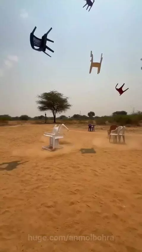 Colorful plastic chairs falling from the sky onto a sandy desert landscape, kicking up dust.