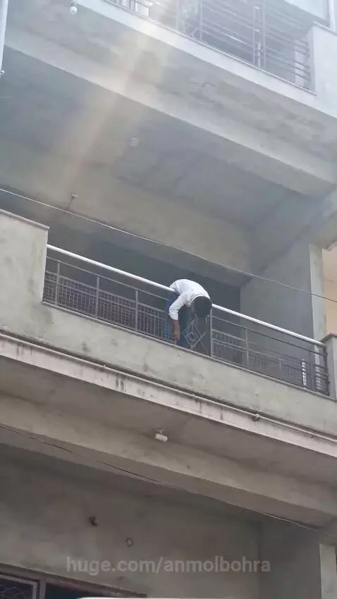 Man on second-story balcony grabbed by a monkey, almost falling over the railing.