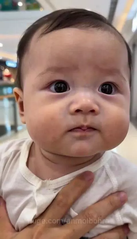Close-up of a baby's face turning red and crying after putting a chili pepper in its mouth.