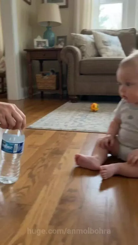 Baby laughing and covering face after winning a bottle flip challenge against an adult.